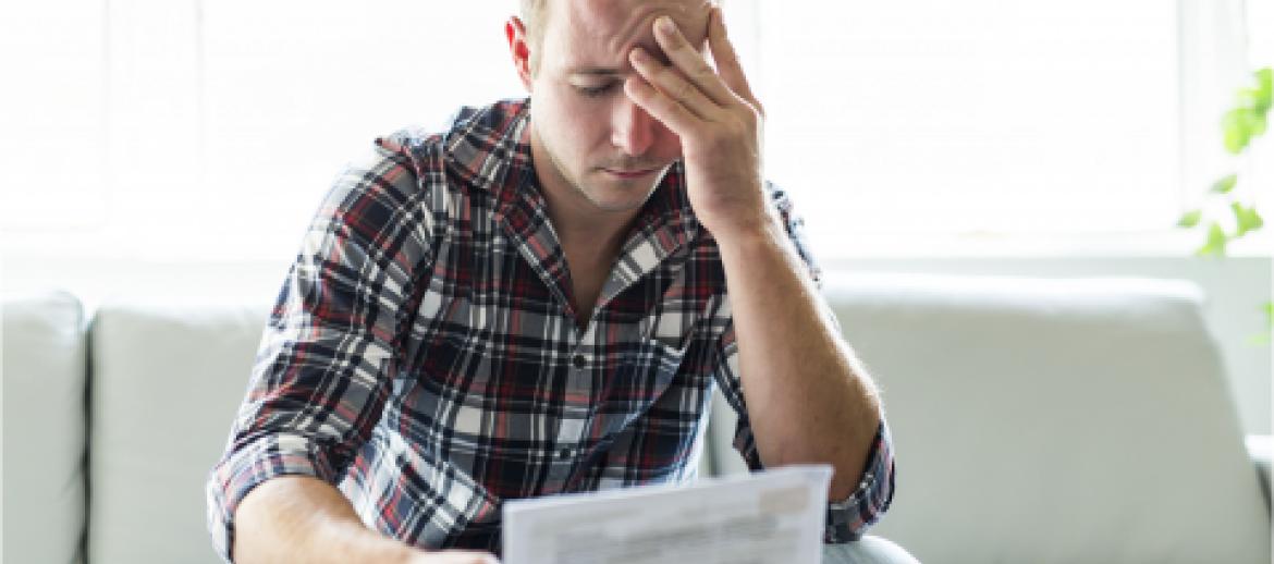 Man worried with head in hands looking at a bill