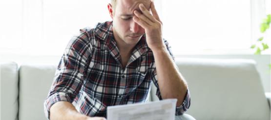 Man worried with head in hands looking at a bill