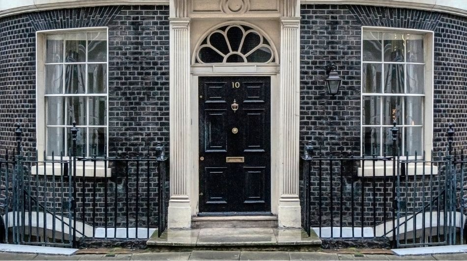 Black door of Number 10 Downing Street in London, with railings black brick wall 