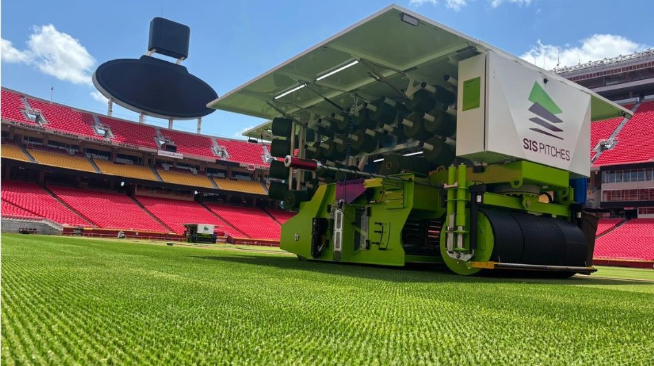 Grounds maintenance machine preparing stadium pitch on bright green football field.