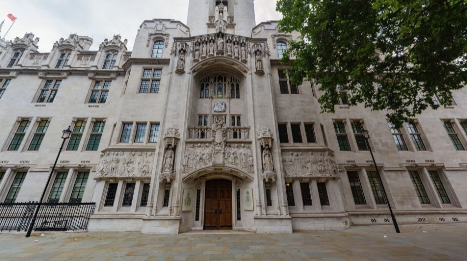 Ornate white stone Supreme Court building façade with arched entrance, carved figures, and tall windows.