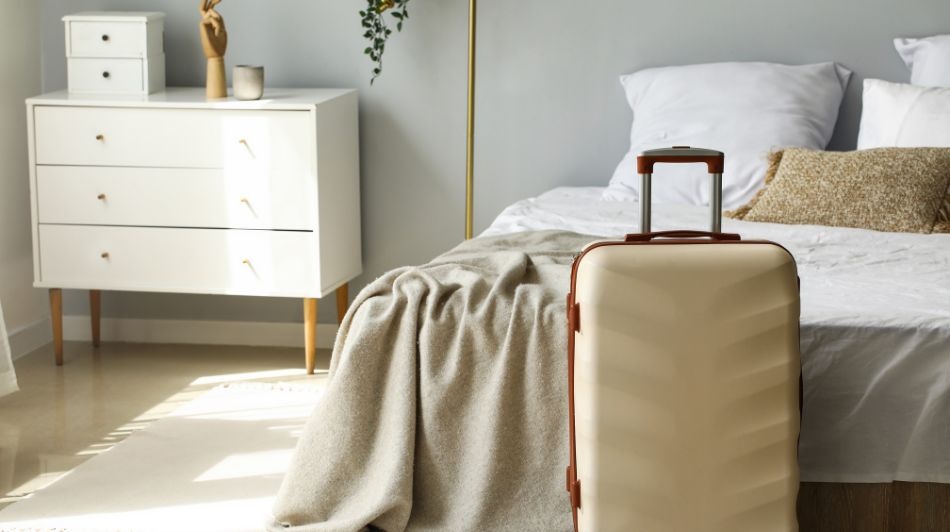 Minimalist bedroom with neatly made bed, soft throw blanket, and suitcase ready for a stay.