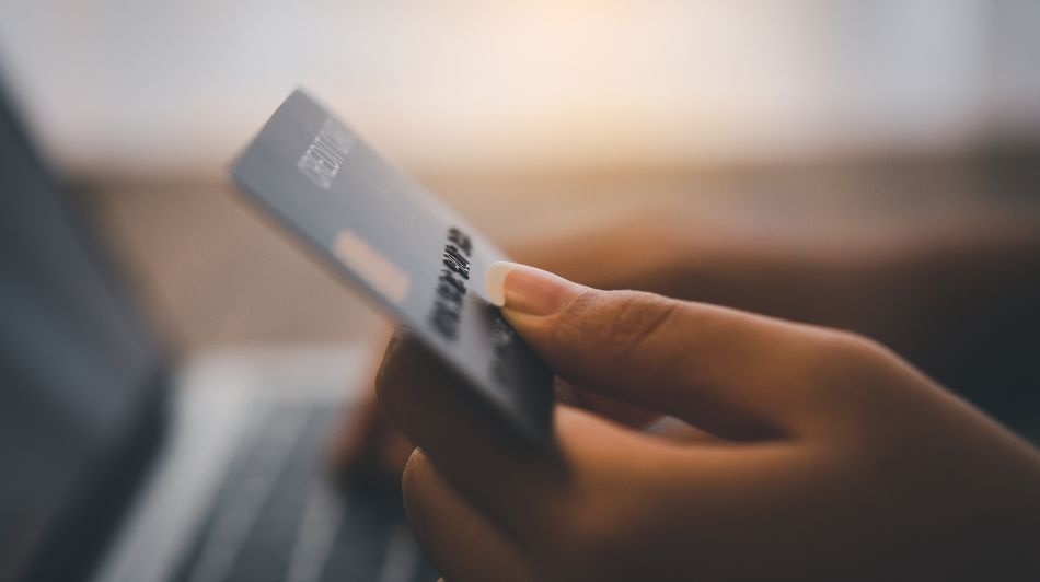 Close-up of a hand holding a payment card while making an online purchase on a laptop.