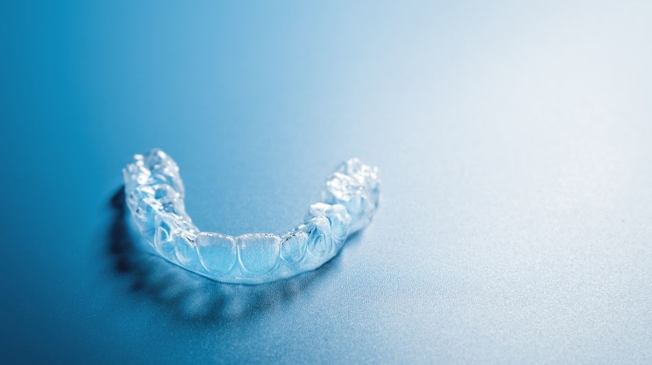 Clear dental aligner tray on a blue surface, used for discreet teeth straightening.