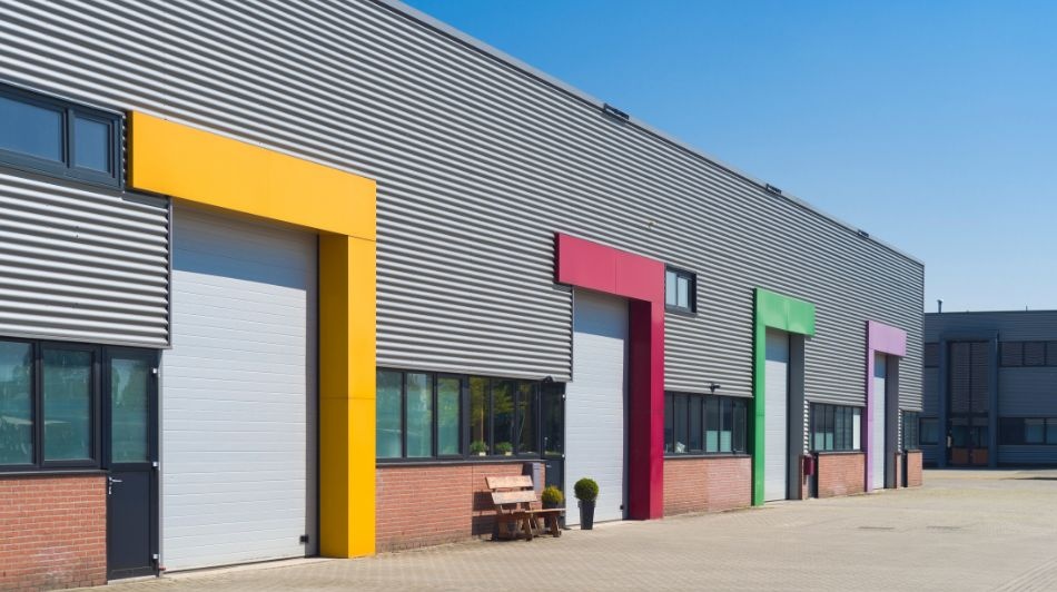 Industrial warehouse units with colourful loading bay surrounds and roller shutter doors on a modern business park.