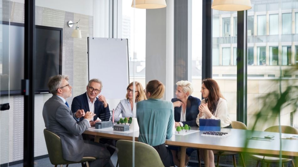 Modern office boardroom meeting with professionals gathered around a conference table and presentation easel.