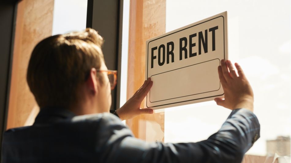 Person placing a “For Rent” sign in a shopfront window, advertising commercial property availability.