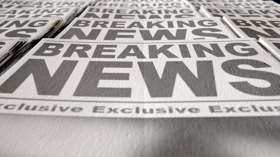 Stack of newspapers featuring large “Breaking News” headlines, photographed from a low angle with selective focus.