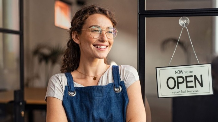 Small business owner in shop with “Now we are open” sign, representing a newly incorporated limited company.