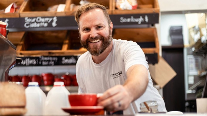 Café barista handing a red coffee cup to a customer over counter with pastries and milk bottles