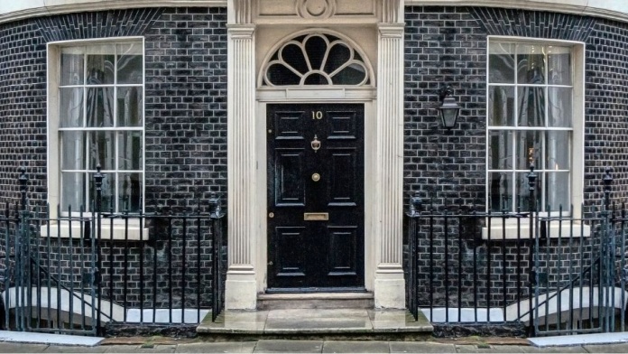 Black door of Number 10 Downing Street in London, with railings black brick wall 