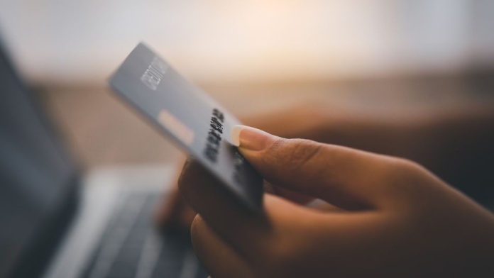 Close-up of a hand holding a payment card while making an online purchase on a laptop.