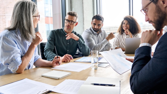 Business professionals collaborating around a conference table during an office meeting with documents and laptops.
