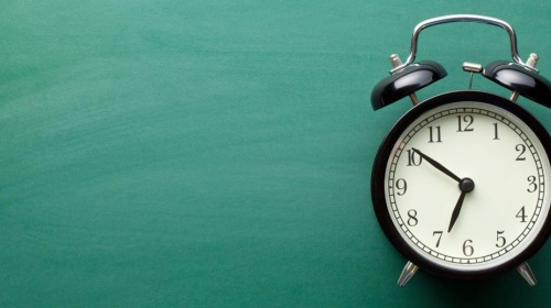 Classic alarm clock resting on a turquoise tabletop against a teal backdrop.