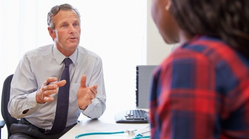 Healthcare professional speaking with a patient across a desk during a medical consultation. 