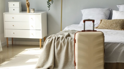 Minimalist bedroom with neatly made bed, soft throw blanket, and suitcase ready for a stay.