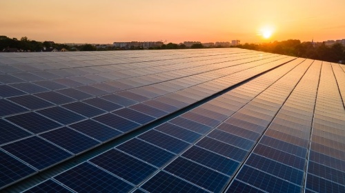 Large solar panel array generating renewable energy at sunset with city skyline in the distance.