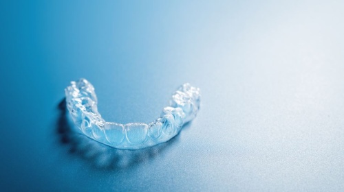 Clear dental aligner tray on a blue surface, used for discreet teeth straightening.