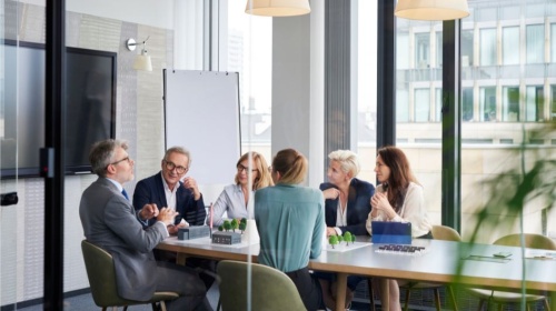 Modern office boardroom meeting with professionals gathered around a conference table and presentation easel.