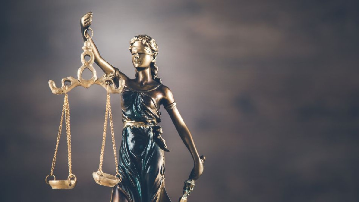 Classical justice statue holding balanced scales against a dark, cloudy background
