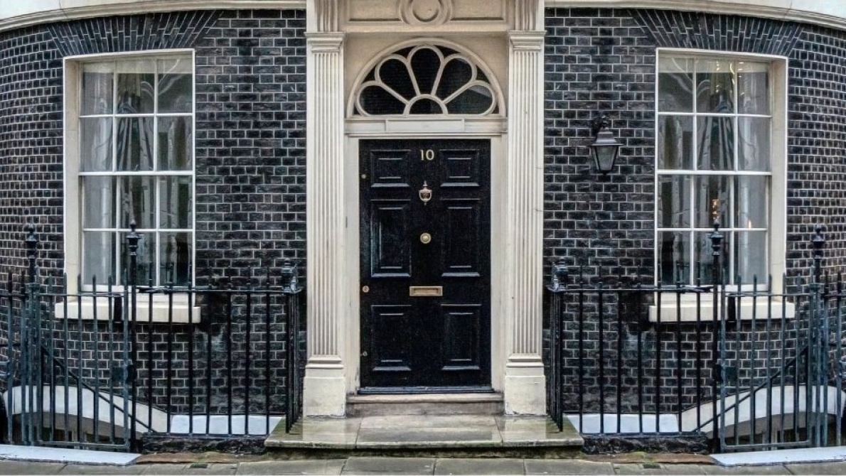 Black door of Number 10 Downing Street in London, with railings black brick wall 