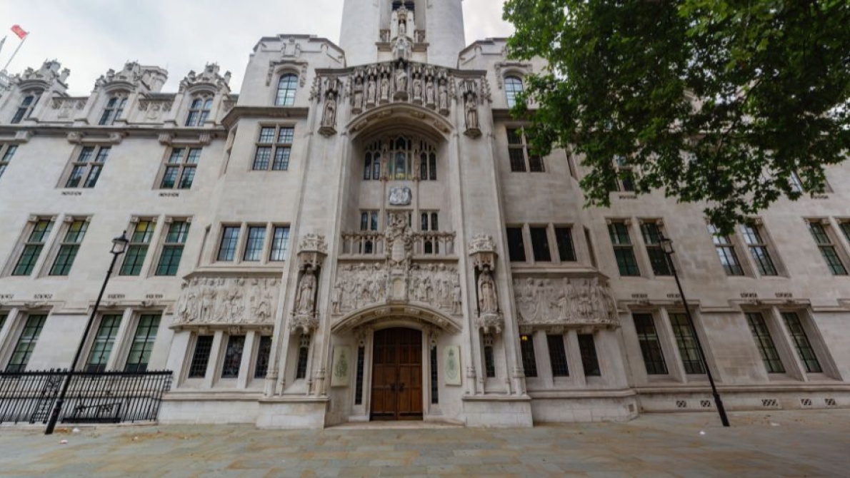 Ornate white stone Supreme Court building façade with arched entrance, carved figures, and tall windows.