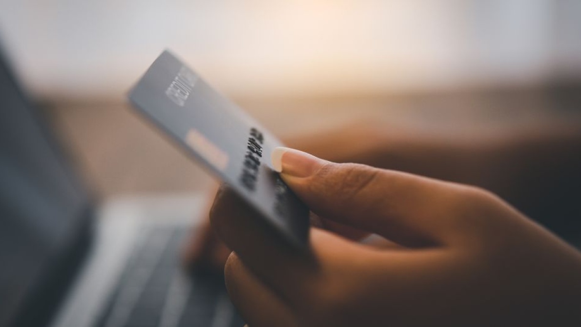 Close-up of a hand holding a payment card while making an online purchase on a laptop.