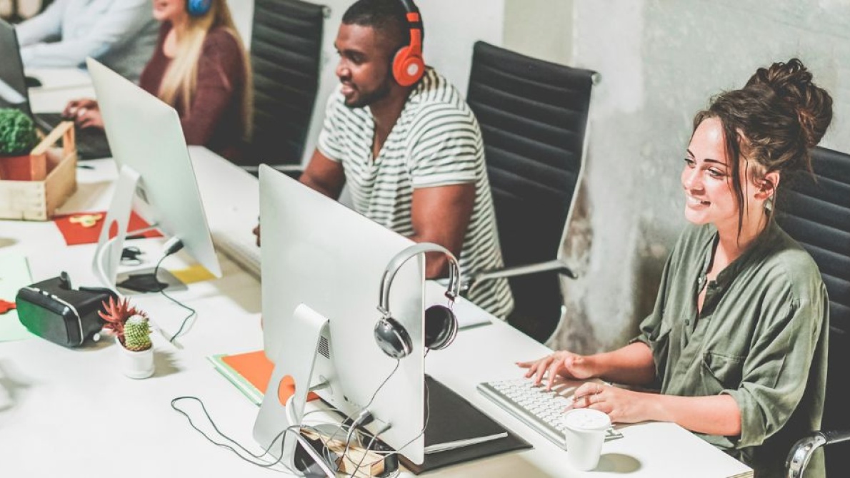 Office workers using desktop computers and headsets in a modern collaborative workspace