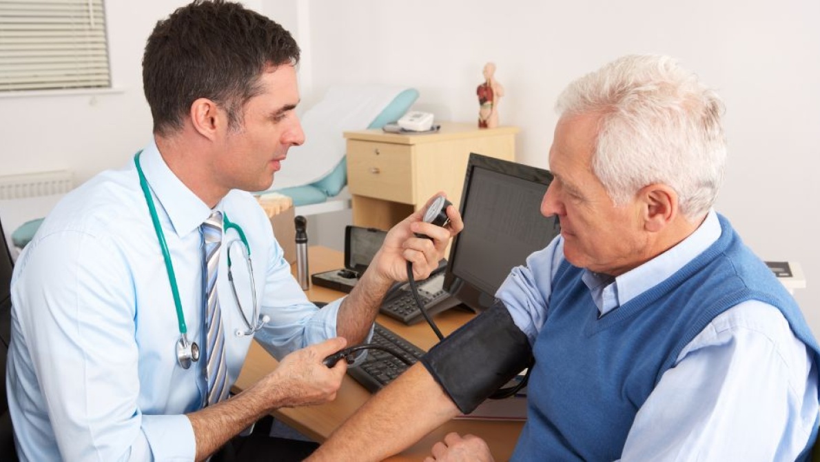 Healthcare professional measuring a patient's blood pressure during a consultation in a medical examination room.