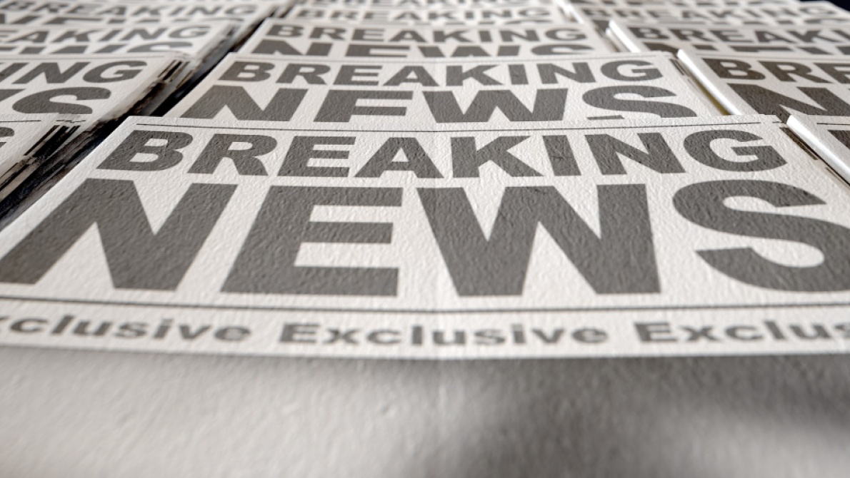 Stack of newspapers featuring large “Breaking News” headlines, photographed from a low angle with selective focus.