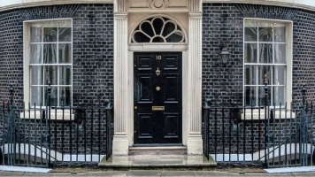 Black door of Number 10 Downing Street in London, with railings black brick wall 