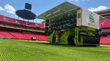 Grounds maintenance machine preparing stadium pitch on bright green football field.