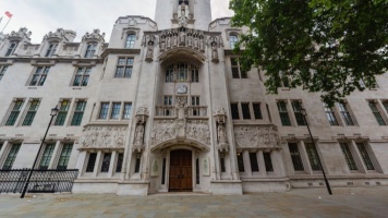 Ornate white stone Supreme Court building façade with arched entrance, carved figures, and tall windows.