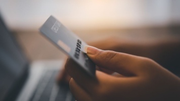 Close-up of a hand holding a payment card while making an online purchase on a laptop.