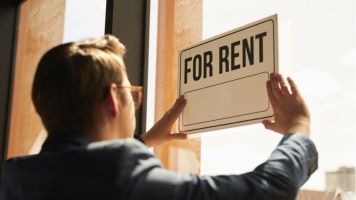 Person placing a “For Rent” sign in a shopfront window, advertising commercial property availability.