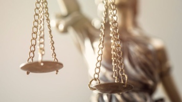 Close-up of golden scales of justice hanging from chains, with a blurred Lady Justice statue in the background.