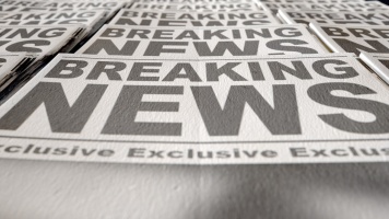 Stack of newspapers featuring large “Breaking News” headlines, photographed from a low angle with selective focus.