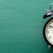 Classic alarm clock resting on a turquoise tabletop against a teal backdrop.