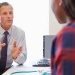 Healthcare professional speaking with a patient across a desk during a medical consultation. 