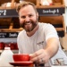 Café barista handing a red coffee cup to a customer over counter with pastries and milk bottles