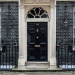 Black door of Number 10 Downing Street in London, with railings black brick wall 