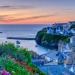 Colourful coastal village at sunset with harbour, boats and flower-lined hillside.