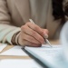 Close-up of a person reviewing documents and signing paperwork with a silver pen at a desk.