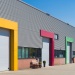 Industrial warehouse units with colourful loading bay surrounds and roller shutter doors on a modern business park.