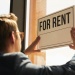 Person placing a “For Rent” sign in a shopfront window, advertising commercial property availability.