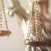 Close-up of golden scales of justice hanging from chains, with a blurred Lady Justice statue in the background.