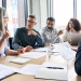 Business professionals collaborating around a conference table during an office meeting with documents and laptops.