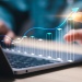 Hand interacting with a digital growth chart projected above a laptop, illustrating business performance, analytics, and financial growth.