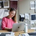 Person working on a laptop at a desk surrounded by fabric swatches and textile samples pinned to a studio wall.