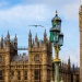The Houses of Parliament and Big Ben in London beneath a cloudy sky, with an ornate Victorian street lamp and birds flying overhead.